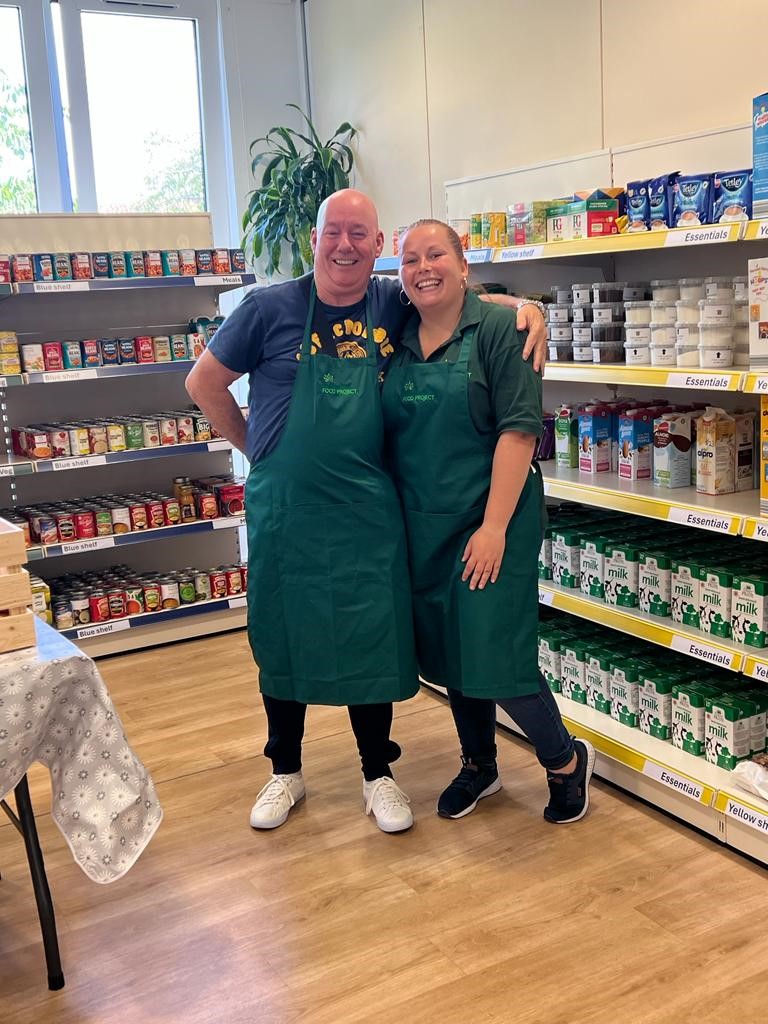 Two people stood in foodbank wearing Edinburgh Food Project aprons. 